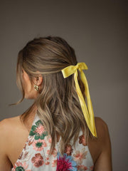 Pinza para cabello con lazo amarillo, fijación estable y cómoda.