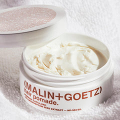 Manos aplicando Malin+Goetz Hair Pomade para volumen y fijación